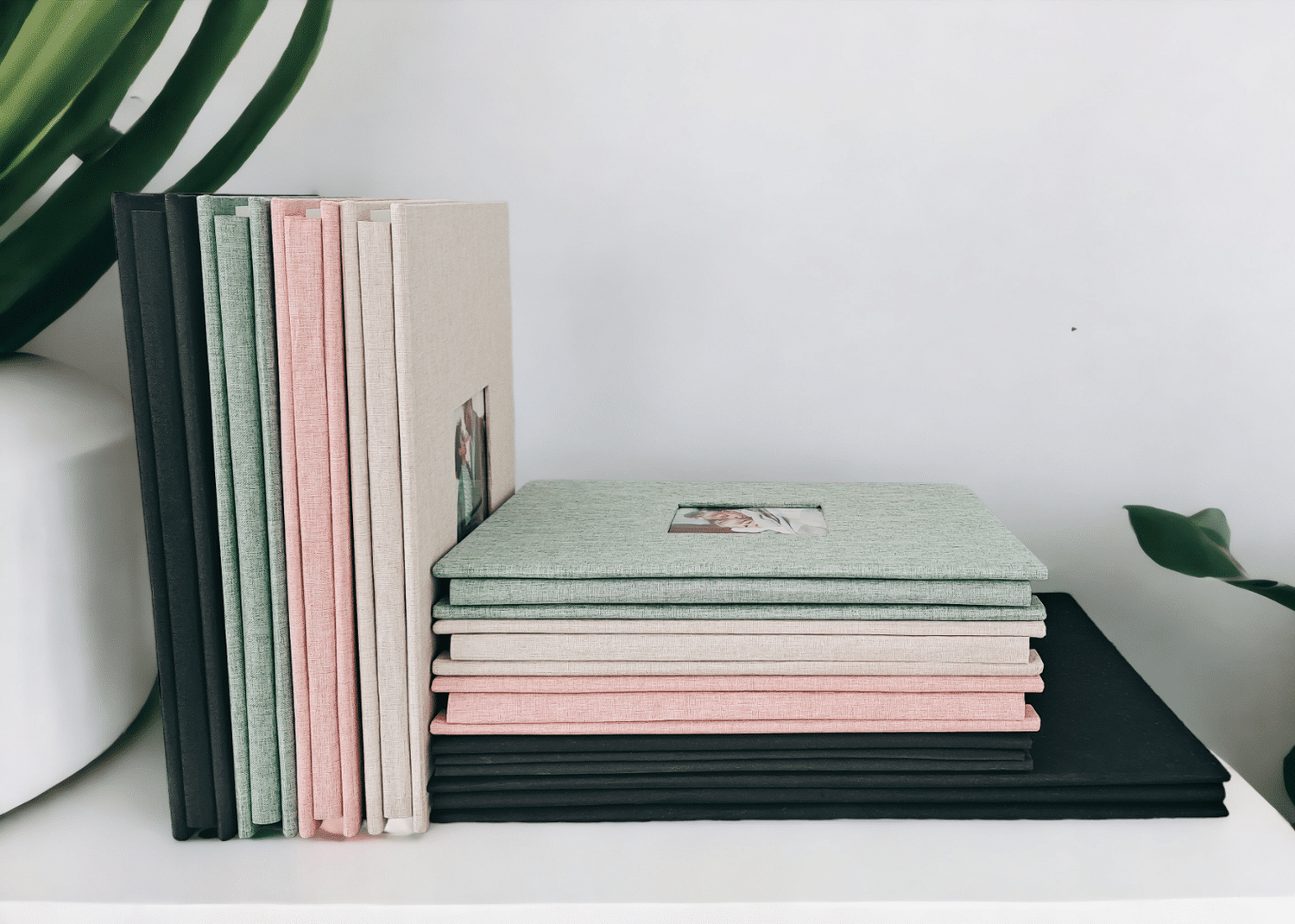 Stack of notebooks in various colors on a white surface with green plants in the background